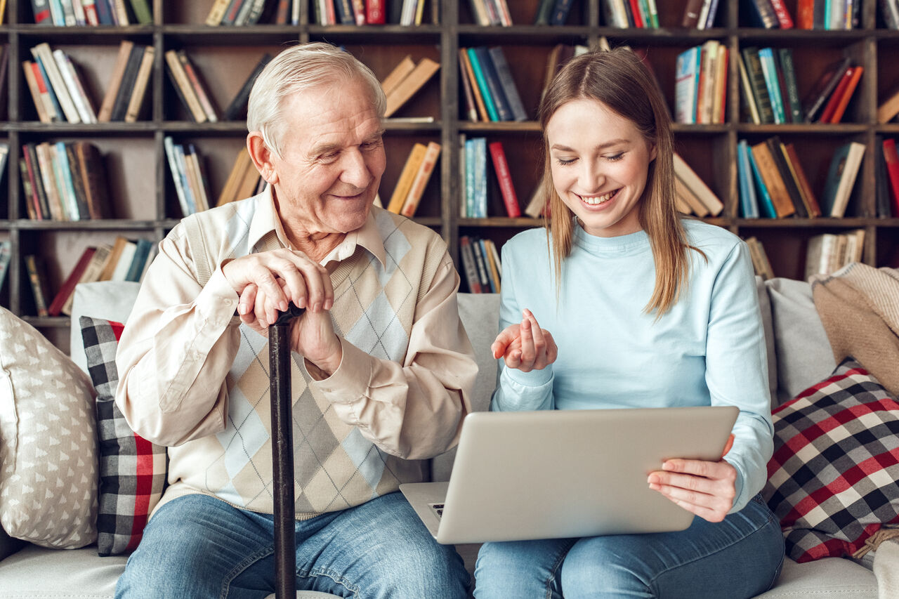 Une jeune femme discute avec un senior et l'aide à faire des démarches informatiques